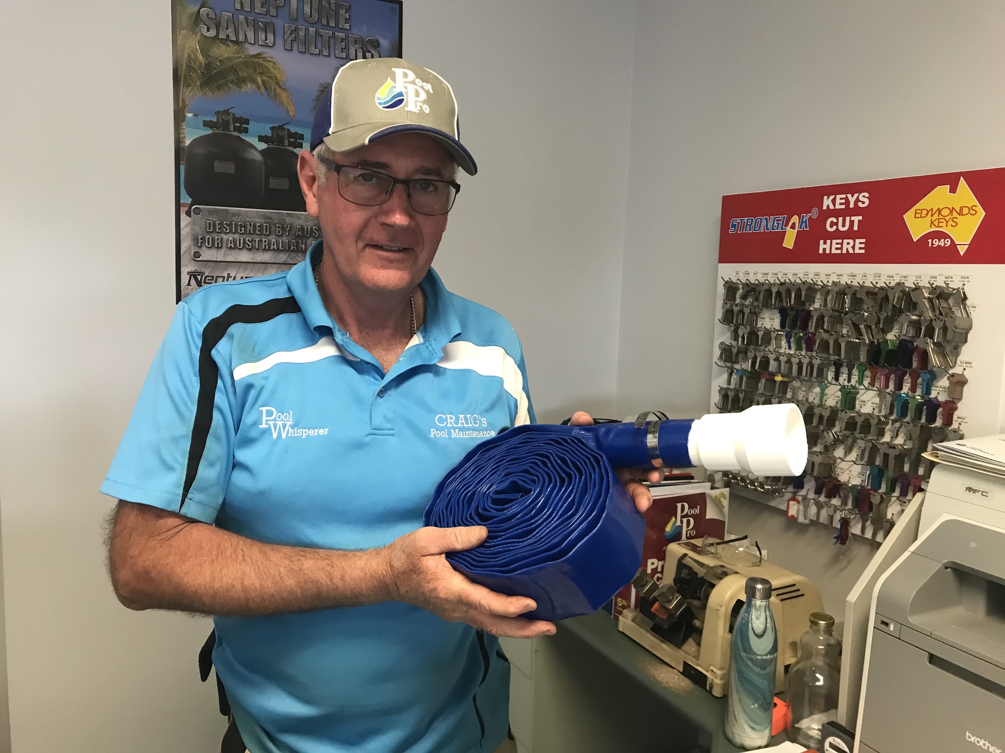 Craig in the Highfields shop wearing his branded Pool Whisperer polo, holding a pool hose fitting