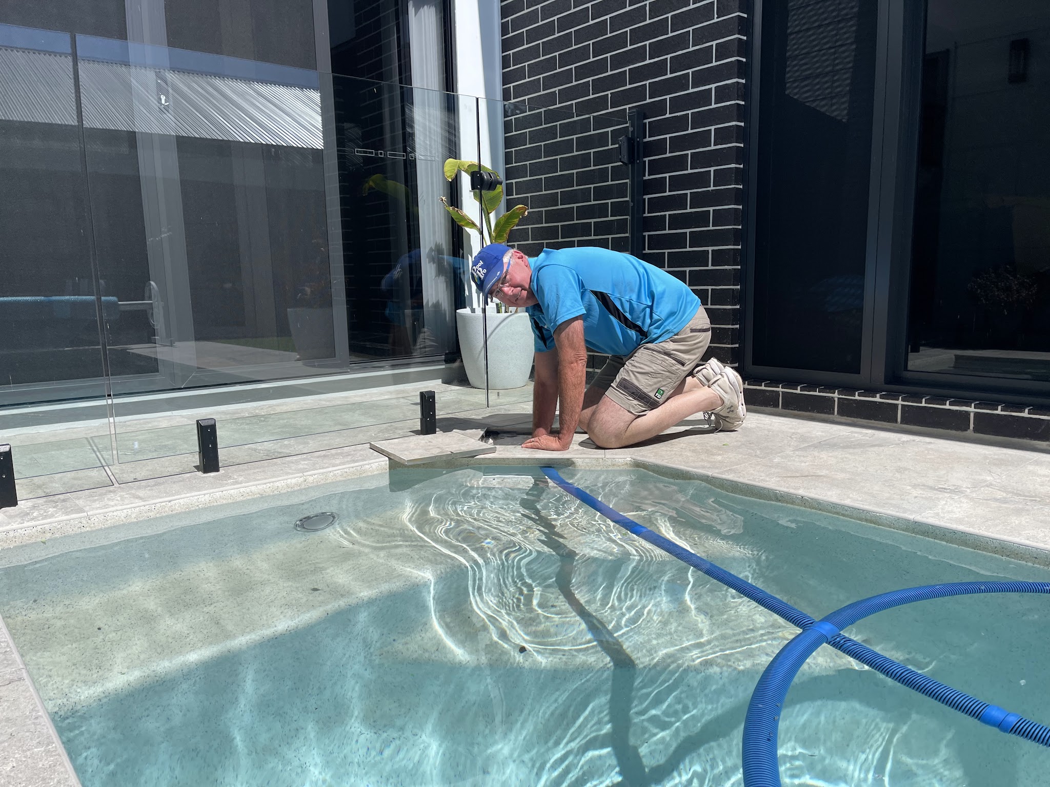 Craig working at a plunge pool beside a modern black brick home with glass pool fencing