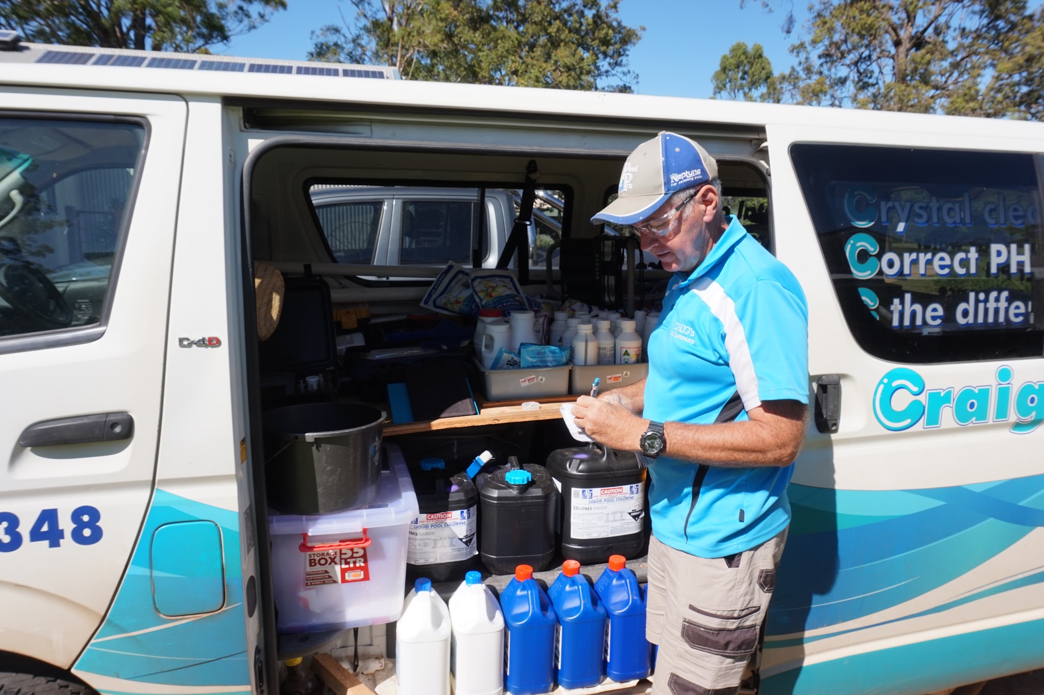 Craig at the open back of his liveried van, writing on a clipboard beside his chemical stock